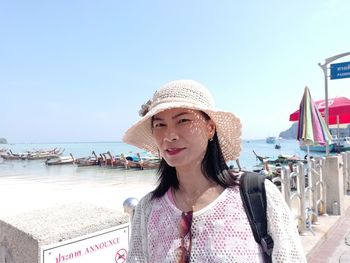 Portrait of woman wearing hat standing at beach against clear sky