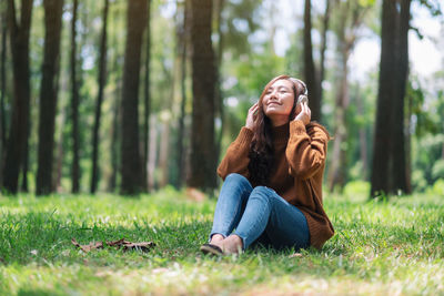 Smiling woman listening to music while sitting on grass