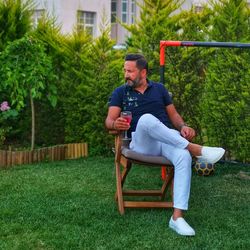 Man holding drink in glass while sitting on chair in yard