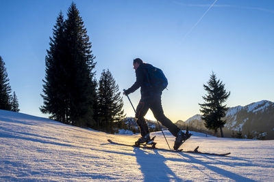 Side view of mature man skiing on snow covered landscape against blue sky during sunset