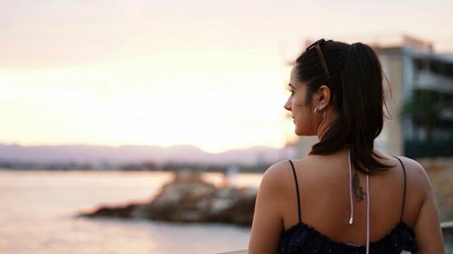Portrait of smiling young woman looking away againts sea at sunset