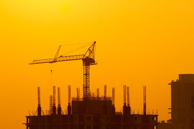 Silhouette cranes at construction site against sky during sunset