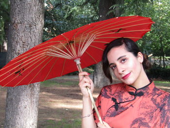 Portrait of woman with umbrella on tree trunk during rainy season