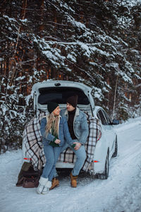 A loving young couple in an embrace sits in the trunk of a white car in winter 