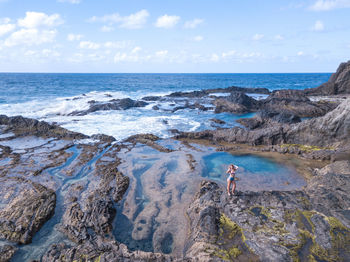 High angle view of woman standing on rock at beach against sky