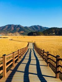 Walkway leading towards mountains against clear blue sky