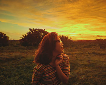 Beautiful woman standing on field against orange sky