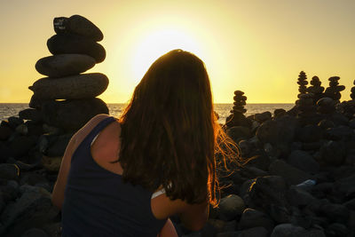 Rear view of woman standing by pebbles at sunset