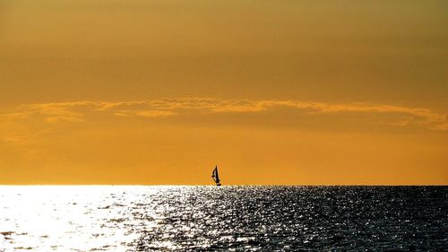 Silhouette person standing by sea against sky during sunset