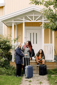 Happy multi-generation family waiting with luggage outside house