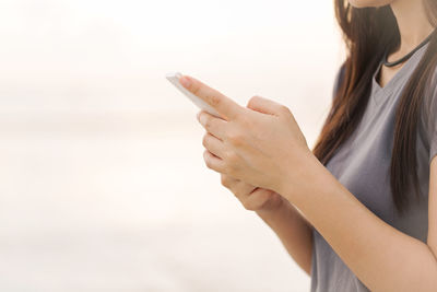 Close-up of woman holding smart phone against sky