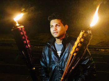 Portrait of young man standing against illuminated fire