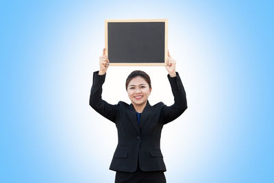 Portrait of smiling businessman holding blank blackboard against blue background