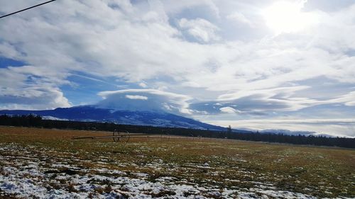 Snow covered field against cloudy sky