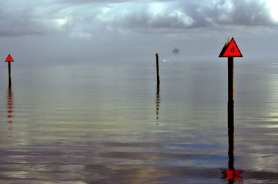 Red wooden post in sea against sky