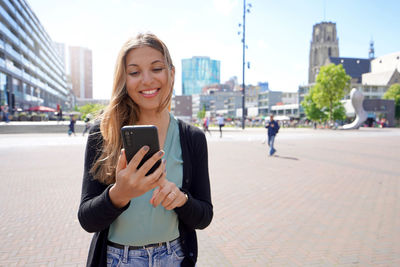 Portrait of young woman using smartphone app in rotterdam modern city square, netherlands