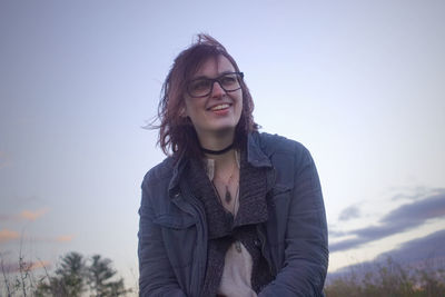 Smiling young woman looking away while standing against sky during sunset