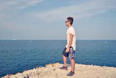 Full length of man standing on cliff by sea against sky