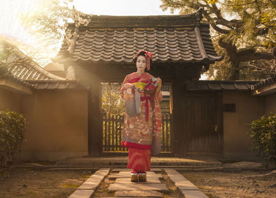 Portrait of woman wearing kimono while standing against built structure