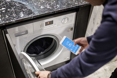 Cropped image of man controlling washing machine with mobile app at smart home