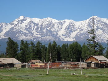 Houses by trees and snowcapped mountains against sky