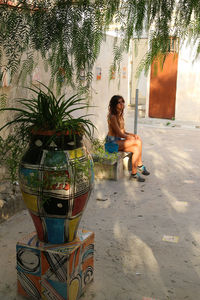 Woman sitting on street against trees in city