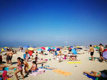 People relaxing at beach against clear sky