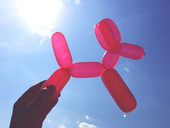 Cropped hand holding dog shaped balloon against blue sky