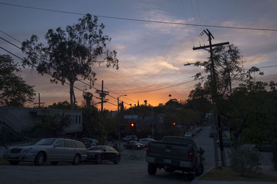 Cars on city street against sky at sunset