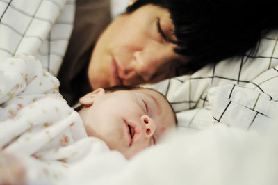 Mother sleeping with cute baby daughter on bed at home