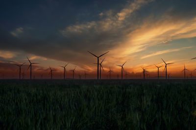 Wind turbines on field against sky during sunset