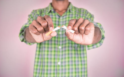 Midsection of man holding cigarette against pink background
