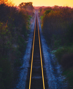 Railroad tracks amidst trees against sky during sunset