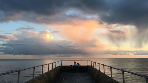 Pier on sea against cloudy sky