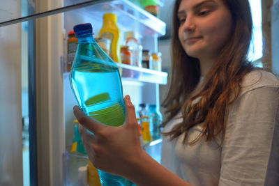 Teenage girl removing bottle from refrigerator