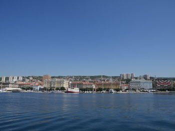 Sea by buildings against clear blue sky