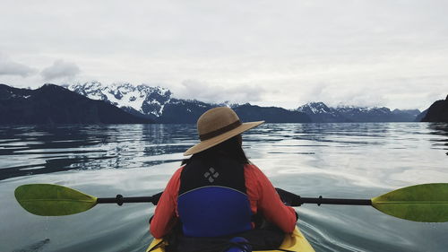 Rear view of woman kayaking in river against mountains during winter
