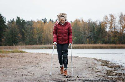Injured woman walking with crutches on the beach looking thoughtful