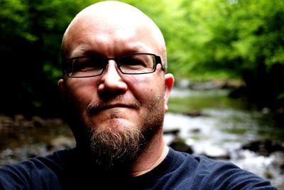 Close-up portrait of man wearing eyeglasses while standing against river