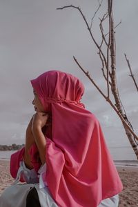 Side view of woman with pink umbrella on beach against sky