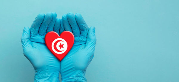 Close-up of hand holding heart shape against blue background