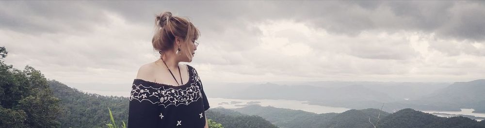 Woman looking away while standing on mountain against sky