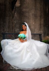 Bride holding flower bouquet while sitting on bench