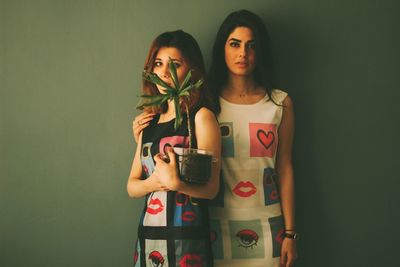 Portrait of women with potted plant standing against wall