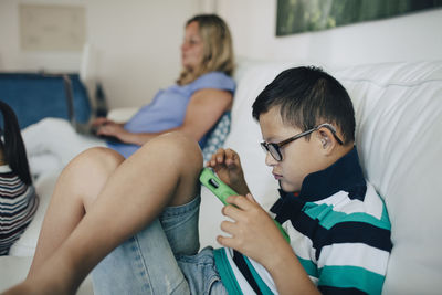 Disabled boy using digital tablet and mother with laptop sitting on sofa