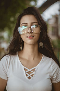 Portrait of young woman wearing eyeglasses while standing against trees