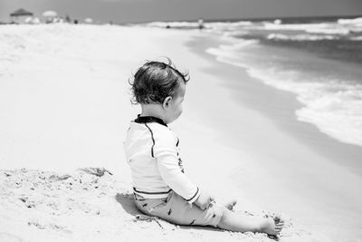 Side view of boy sitting on shore at beach during sunny day