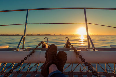 Low section of person relaxing by railing against sky during sunset