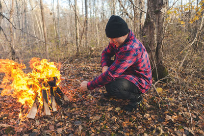 Full length of man crouching by campfire in forest during autumn
