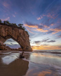 Rock formation on beach against sky during sunset